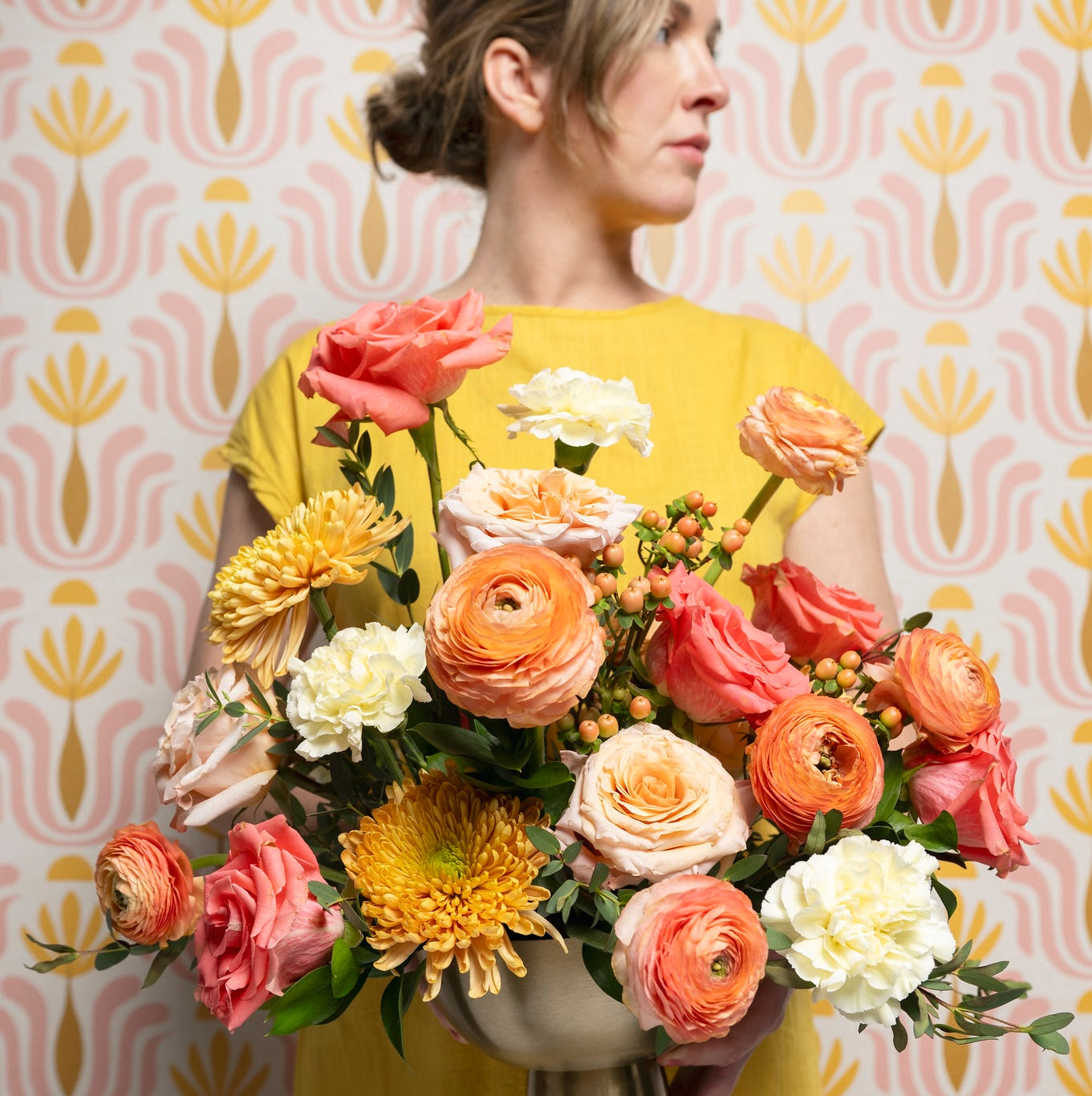 Woman holding a large bouquet of flowers against a patterned wall.